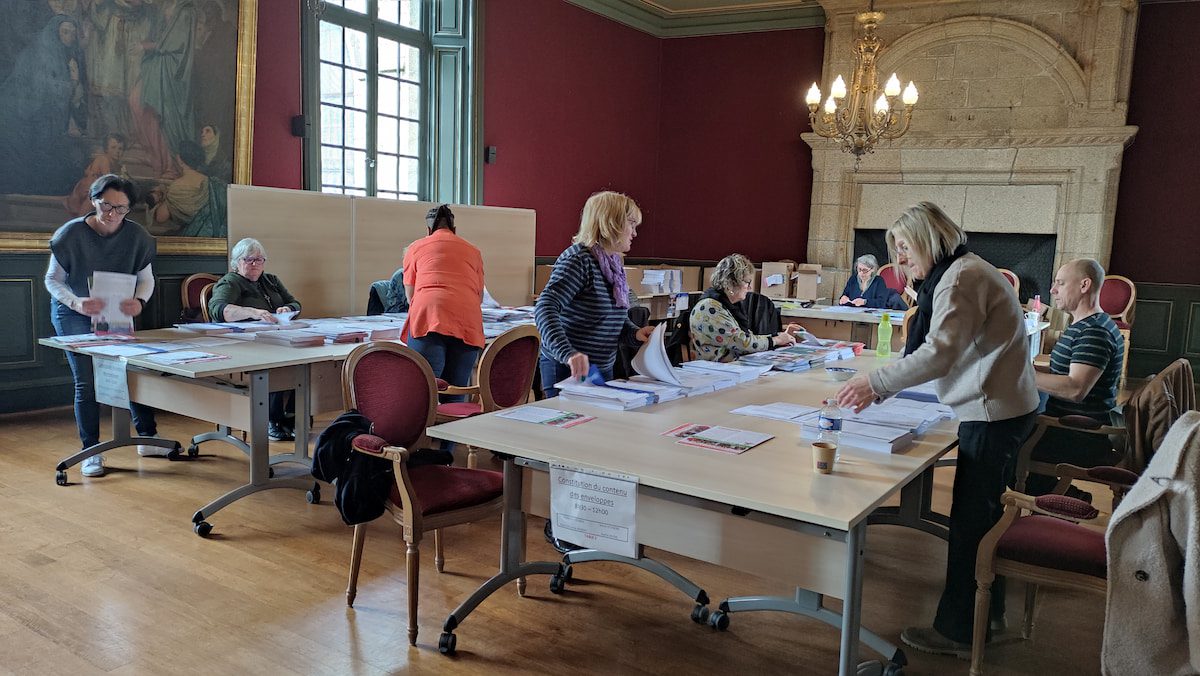 Plusieurs personnes autour de tables en train de constituer les piles de bulletins.